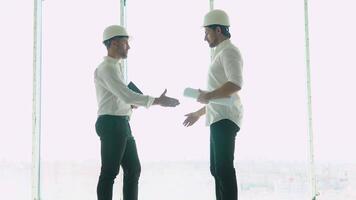 Two engineer with a drawing in hand looking at the construction site. View from the back. Chief Engineer with blueprint in hand looking at the construction video