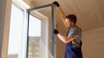 Builder worker in uniform installing pvc window with measure tape in wooden prefabricated house video