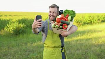 exitoso granjero que lleva cesta de verduras en un soleado día hace un selfie video