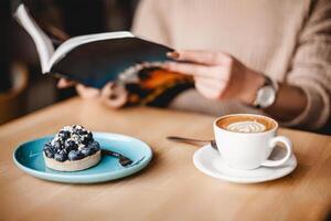 un sereno escena se despliega como un mujer se complace en un libro, acompañado por un encantador arándano tarta y un humeante taza de café, creando un calentar y atractivo ambiente foto