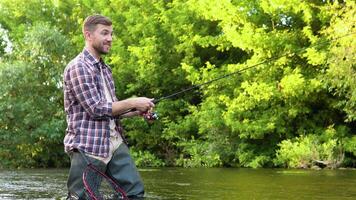 een visser gooit een visvangst hengel staand kniediep in de water van de rivier. vlieg visvangst voor forel. zomer vakantie en mensen concept video