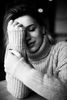 A solitary moment captured as a woman, clad in a cozy sweater, sits with hands on her face, conveying a sense of introspection and melancholy in a serene atmosphere photo