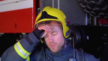 Close up portrait of strong serious fireman in helmet and full equipment standing next to car with flashing lights on and looking into camera video