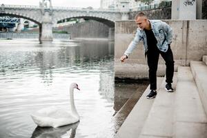 un hombre es alimentación un cisne por el agua foto