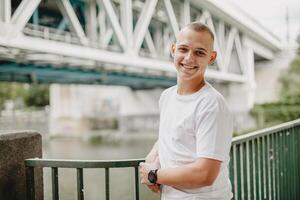 A man is smiling and posing for a picture in front of a bridge photo