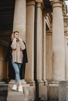 mujer en marrón Saco en pie en frente de ciudad edificio con columnas concepto de urbano paisaje con elegante hembra figura urbano Moda y arquitectura. capturar urbano estilo de vida y diseño elementos foto