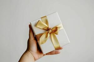 Elegant hand holding white gift box with gold ribbon isolated on solid background. Stock photo. photo