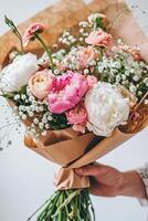 Luxurious floral arrangement featuring peonies, ranunculus, and baby's breath in brown kraft paper wrapping. photo