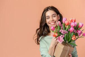 Happy mom celebrates Mother's Day with gifts and flowers against a peach backdrop. photo