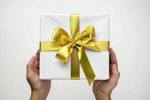 Chic hand holding white gift box with gold ribbon isolated on solid background. Stock photo. photo