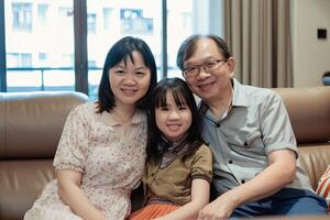 Asian family of three smiling together on sofa at home. Happy domestic scene. photo