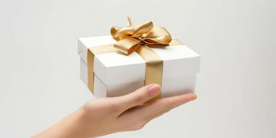 Hand holding white gift box with gold ribbon on white background. Product photography. photo