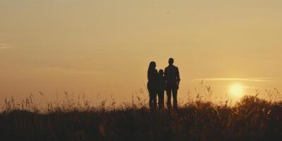 Silhouetted family of four on grassland against warm sunset sky photo