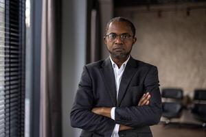 Professional middle-aged businessman with glasses standing confidently with arms crossed in a modern office setting. photo