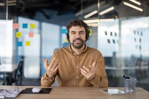 sonriente masculino profesional con auriculares atractivo en un negocio conversacion en un contemporáneo espacio de trabajo con pegajoso notas en antecedentes. foto