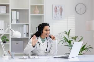 Cheerful female doctor engaging in a pleasant conversation on a headset during a virtual consultation. She is smiling and waving, creating a welcoming atmosphere in her office. photo