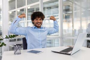 An exuberant professional triumphantly raises their fists in a modern office setting, celebrating a successful business achievement. photo