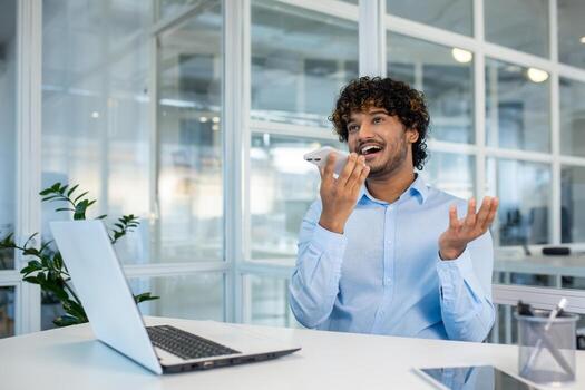 alegre joven masculino profesional disfrutando un alegre conversacion en su teléfono inteligente en un brillante y moderno oficina ajuste. foto