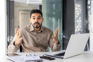 trastornado y decepcionado empresario mirando a cámara a lugar de trabajo tiene negativo financiero resultados, retrato infeliz hombre trabajando dentro oficina a lugar de trabajo con ordenador portátil. foto