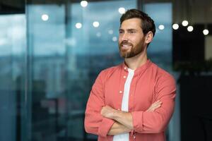 Portrait of a successful businessman inside the office, the man is smiling and looking towards the window, with his arms crossed. photo