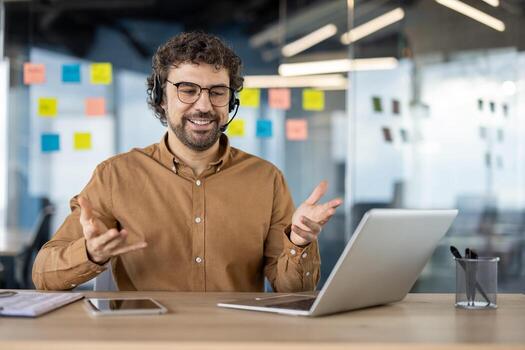 un contento barbado hombre vistiendo auriculares negociaciones alegremente en un conferencia en un moderno oficina ajuste. foto