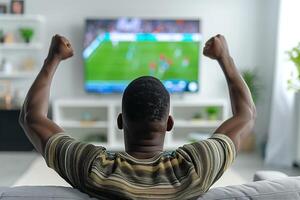 A man sits on the sofa with his back facing the TV, which is showing a football match photo