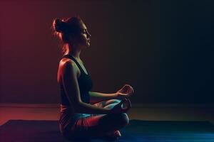 young woman in sportswear is meditating in lotus position in dark room photo