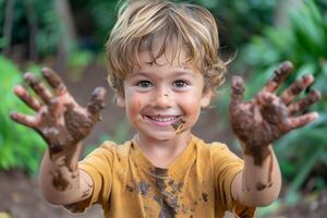 pequeño chico con un alegre expresión demostración ambos de su sucio palmas con suelo pega a ellos foto