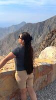 Happy asian woman tourist raise hands enjoys breathing fresh air high in cloudy mountains at cold weather. Young hiker at amazing hazy background of mountain landscape standing back. Active sport. video