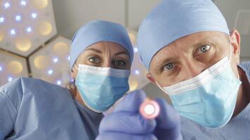 Doctor surgeon with assistant checks the reaction of the pupils of the eyes with bright light. Patient wakes up after a coma. video