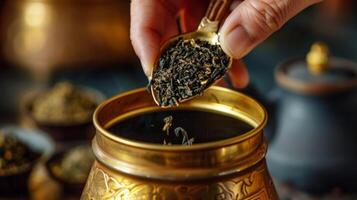 A hand holding a small metal s scooping tea from a golden tin into a pot for brewing photo