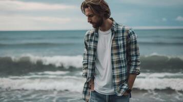 un casual y cómodo Mira presentando un tartán camisa en capas terminado un camiseta y estilizado con afligido mezclilla y zapatillas. el playa y estrellarse olas en el antecedentes anuncio foto