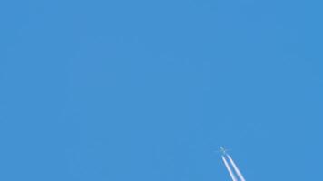 A jet airliner climbs through a vibrant blue sky, leaving a contrail. Airplane in the sky, long shot video