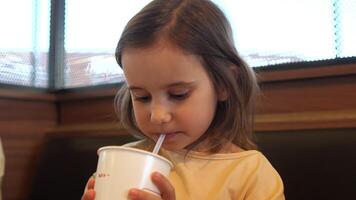 närbild av en liten flicka dricka soda från en sugrör och äter skräp mat video