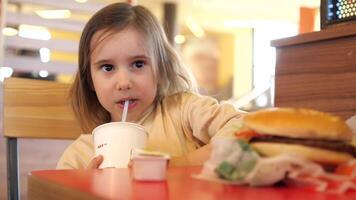 de cerca de un niña Bebiendo soda desde un Paja y comiendo basura comida video