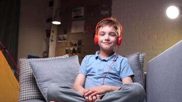 medium shot of a boy sitting on sofa and listening to music with red headphones video