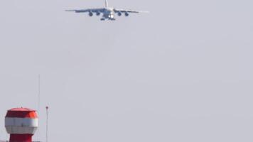 A cargo airplane descends toward an airstrip, its silhouette looming in the haze. Four engine heavy transport airliner landing, front view video