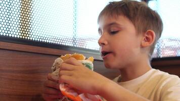 de cerca de un chico comiendo un grande hamburguesa. hambriento niño come un hamburguesa con apetito video