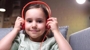 detailopname, portret van een weinig meisje in oranje hoofdtelefoons luisteren naar muziek- video
