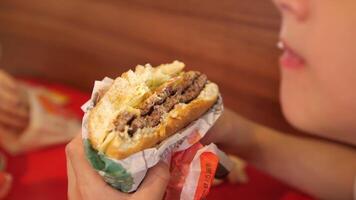 fermer garçon mord une Burger. le garçon mâche une mordu Burger avec enthousiasme. video