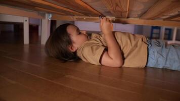 en liten flicka gömde sig under de säng till Kolla på de på de telefon video