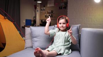 pequeno menina escuta para música dentro laranja fones de ouvido e danças video