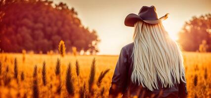 blonde woman in cowboy hat and leather jacket in wheat field at sunset and mountain view, back view, banner photo