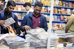 Delhi, India, February 17 2024 - Various age group people reading variety of Books on shelf inside a book-stall at Delhi International Book Fair, Books in Annual Book Fair at Bharat Mandapam complex photo