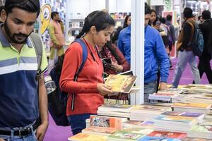 Delhi, India, February 17 2024 - Various age group people reading variety of Books on shelf inside a book-stall at Delhi International Book Fair, Books in Annual Book Fair at Bharat Mandapam complex photo