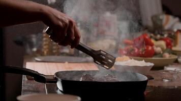 Cook uses metal tongs to adjust a piece of meat on a frying pan and then adds oil cooking. Close up. Slow motion. 4k. video