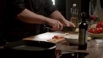 Masculin chef est couper patates avec précision sur un esthétiquement plaisant Coupe planche. là est une bouteille de rouge du vin proche, et divers des légumes pour cuisine sont épars autour. moyen tir. lent mouvement. 4k. video