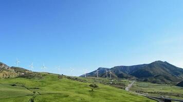 Wind turbines energy moving at field together a road and mountains at sunny day video