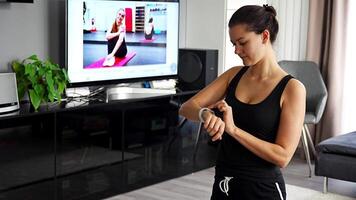 jovem mulher olhando às ginástica rastreador exibindo coração avaliar, passos contagem e queimado calorias. inteligente Assistir em fêmea mão, ponto do visualizar, conceito do ficando em forma às lar. Alto qualidade 4k cenas video