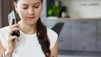 Young woman listening to a voice message on her smartphone while sitting on the couch at home. High quality 4k footage video